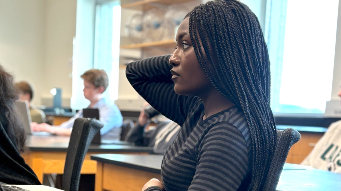 A student in a classroom listens to a speaker. 