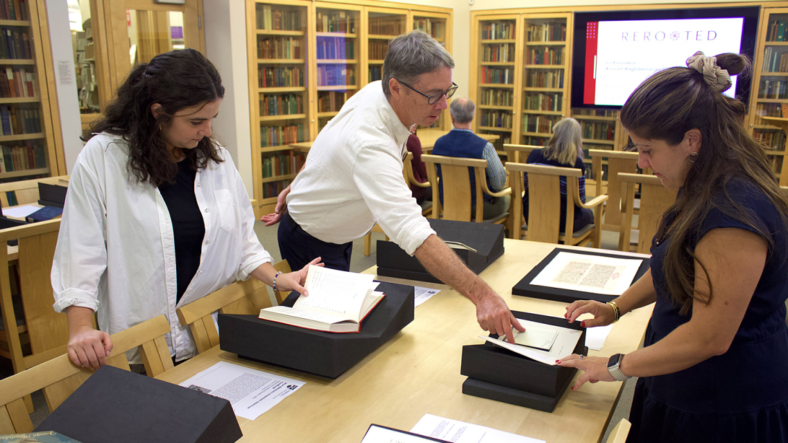 Three people examine printed material in a library special collections area.