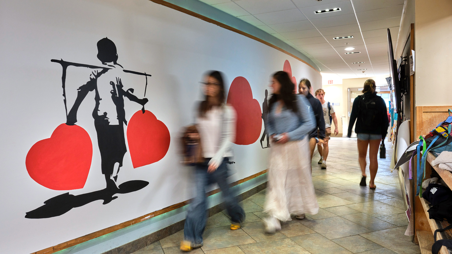 Students walk by a brightly painted indoor mural on a curved wall.