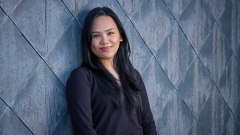 Photo of a student in a dark shirt leaning against a patterned wall outdoors.