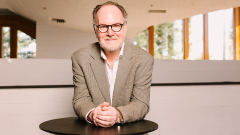 Photo of Professor Peter Matthews smiling and leaning on a table.