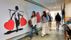 Students walk by a brightly painted indoor mural on a curved wall.