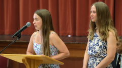 Two students stand at a podium to deliver remarks at a ceremony.