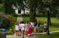A group of people walk across a tree-lined college campus.