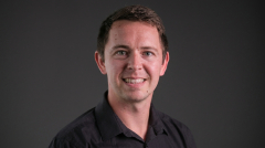 A professor in a dark shirt smiles at the camera.