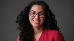 Head shot of a professor wearing read top and glasses smiling at the camera.