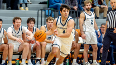 A basketball player drives down the court with his team in the background.