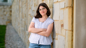 Photo of a student leaning against a stone wall and looking at the camera.