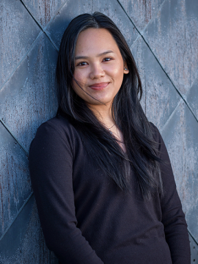 Student wearing dark shirt leans against a patterned wall outside.