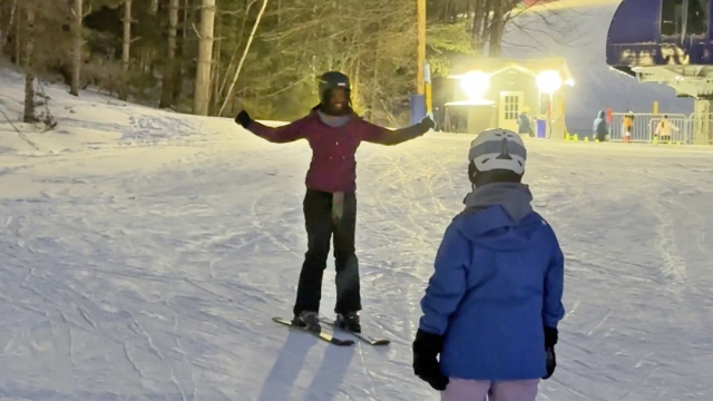 A student skiing down the slope holds up their arms in celebration.
