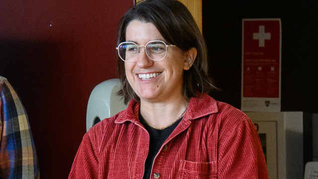 A person with dark hair and glasses in red shirt smiles off camera.