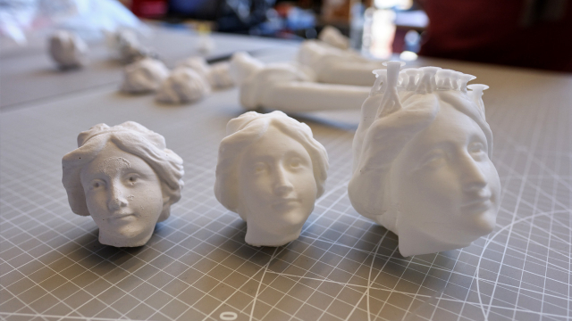 Three small white plaster heads sit on an art bench.
