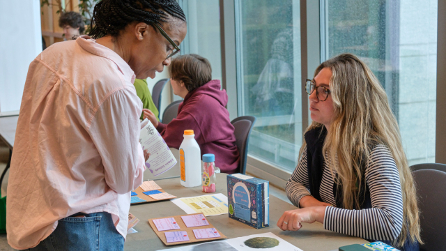 Two students talk to each other over a table at an exhibition.