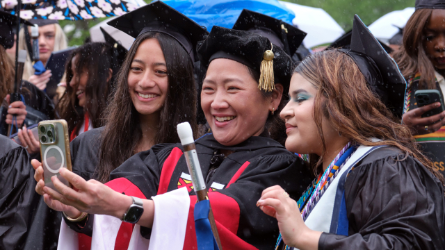 Two students and a professor take a selfie at Commencement.