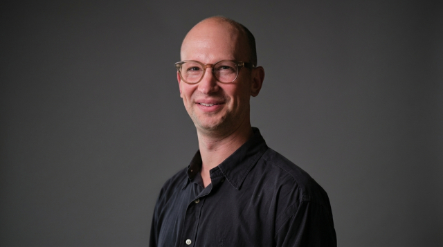 A professor in a black shirt and glasses smiles at the camera.