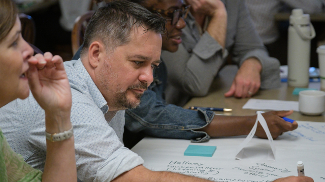 A professor in a white shirt writes on a large paper during a breakout session.