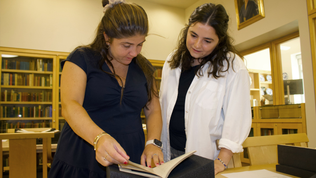 Two people look at a book in a special collections area of a library.