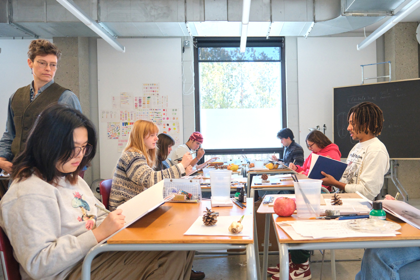 Students sketch botanical objects on a classroom table.