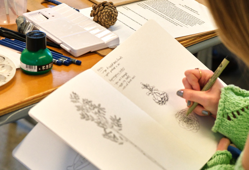 Over the shoulder photo of a student sketching in a book.