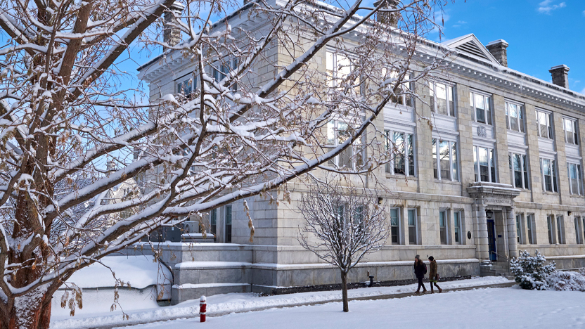 Students walk by a large campus building on a snowy day.