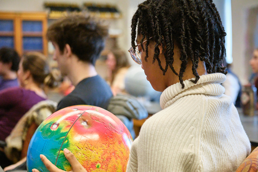 A student looks at a colorful planet model in a classroom.