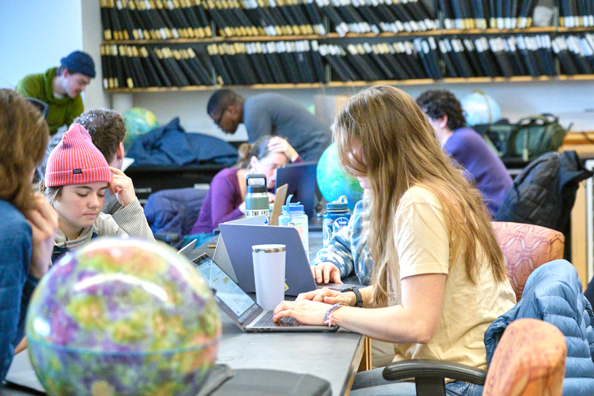 A student works at a laptop in a science lab surrounded by other students.