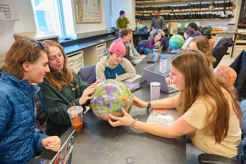 Students look at a model of a planet at a classroom table.