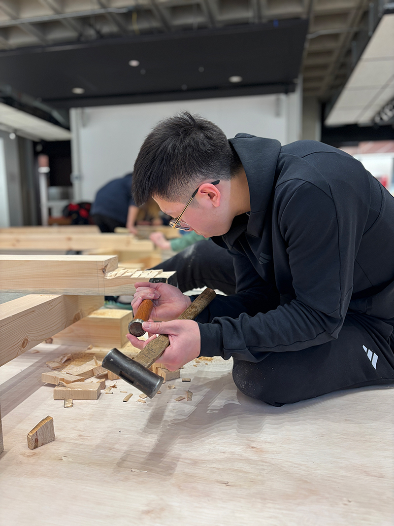 A student works on a timber with chisel and hammer