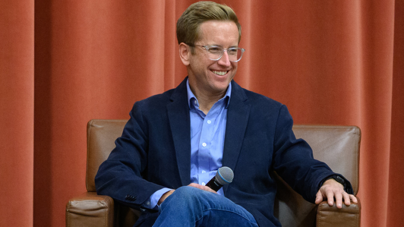 Person in blue dress shirt and jacket smiles on a stage.