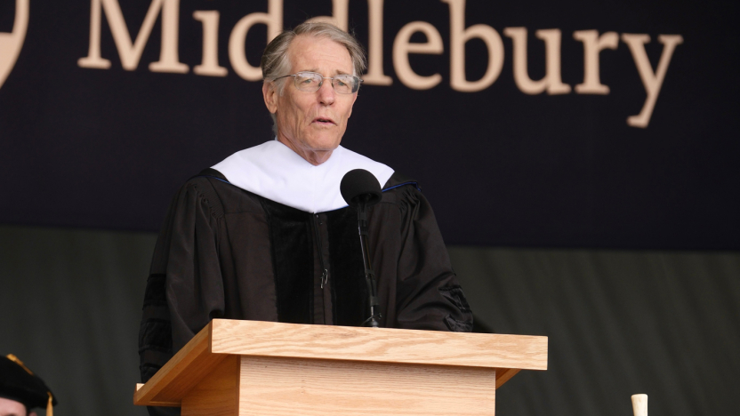 A man wearing academic regalia stands at a podium with a Middlebury banner behind him.