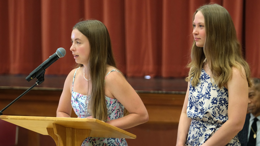 Two students stand at a podium to deliver remarks at a ceremony.