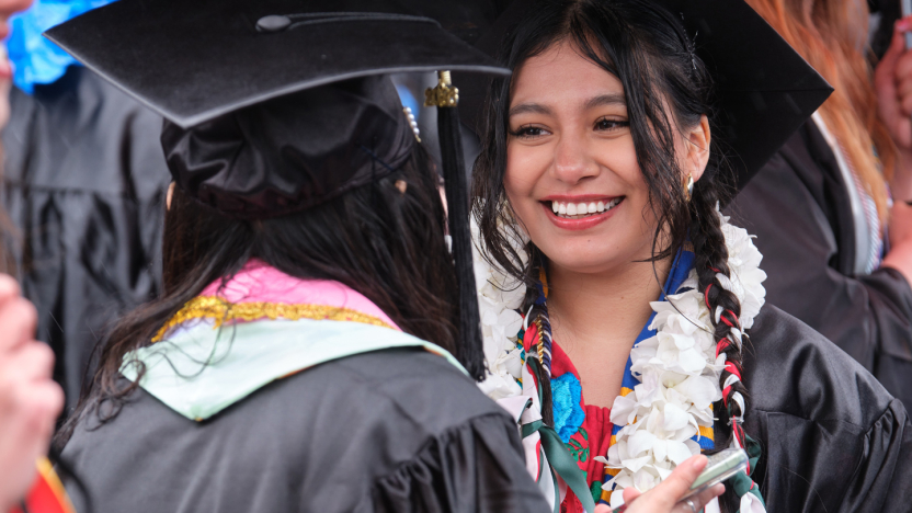 Student wearing graduation cap and gown with lei.