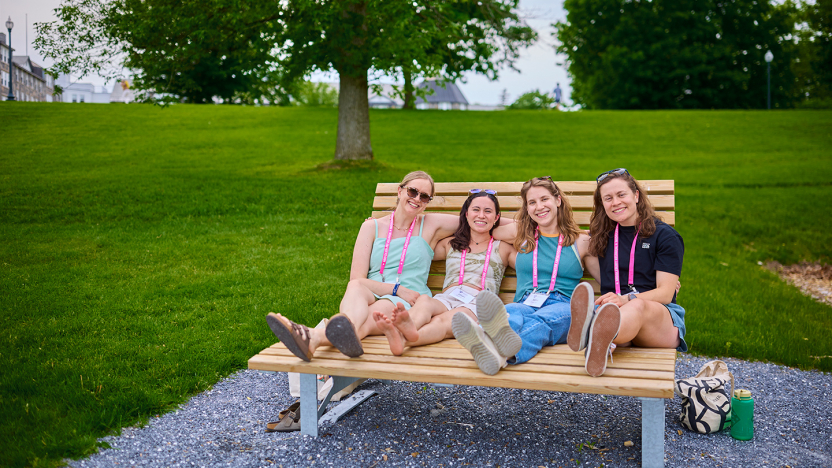Four Reunion attendees recline side by side on a large playground bench on campus.