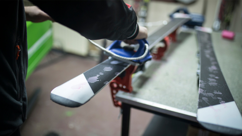 A pair of hands waxes skis on a work table.