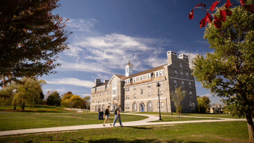 Students walk on a sidewalk with a large residence hall building in the background.