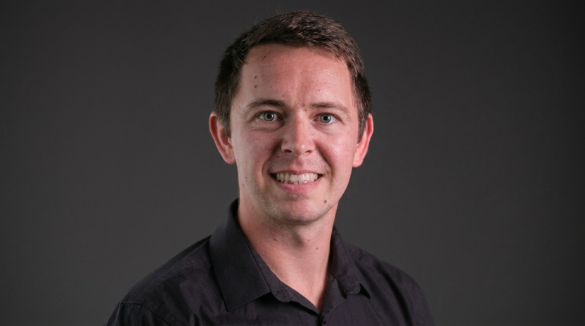 A professor in a dark shirt smiles at the camera.