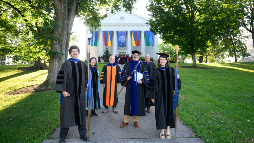 Professors and administrators in academic regalia smile for a group photo outside Middlebury Chapel.