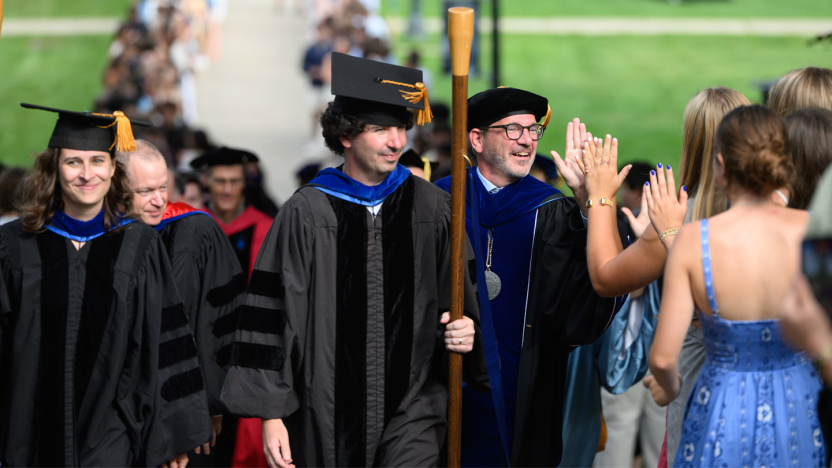 Faculty in academic regalia process outdoors to convocation ceremony