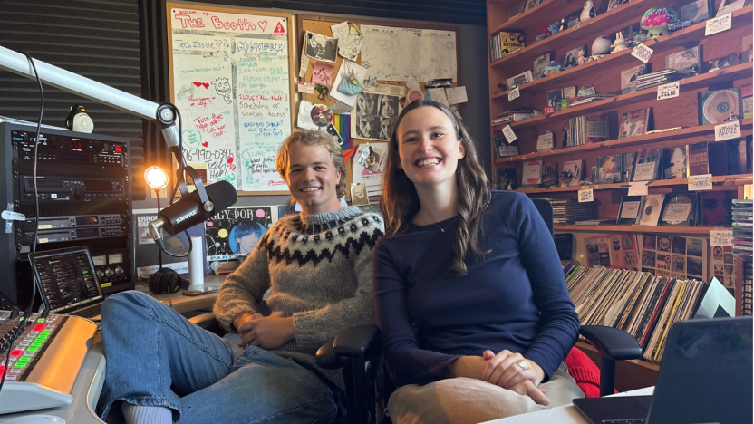Two students sitting in radio studio smile to camera