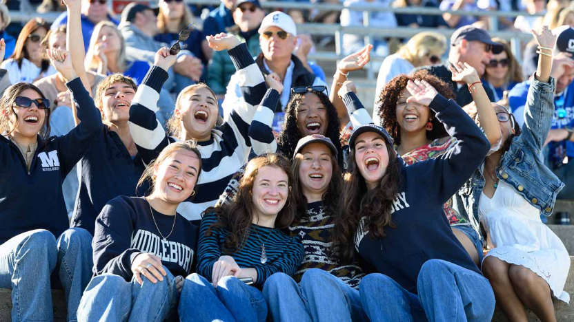A group of spectators cheers from the bleacher seating at the Middlebury football stadium