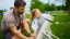 An adult and young child load a t-shirt cannon on a grassy lawn.