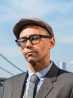 Victor LaValle outside with blue sky looks at camera